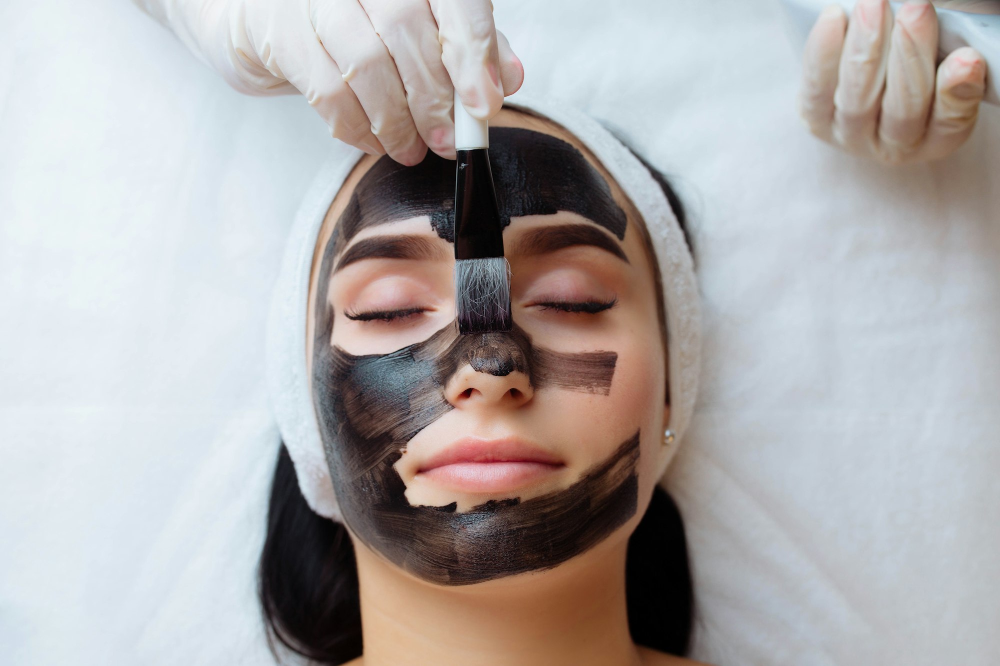 cosmetologist applying black mask on a woman face