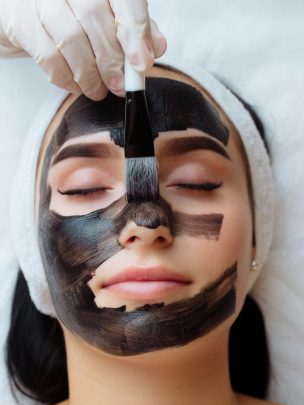 cosmetologist applying black mask on a woman face